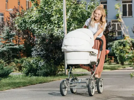 Uśmiechnięta mama spaceruje z białym wózkiem, który jest wyposażony w praktyczne akcesoria.