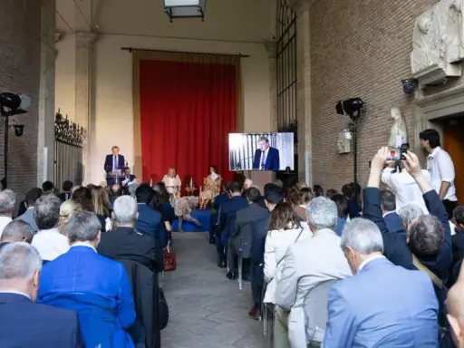 Un evento per il meeting per l'amicizia fra i popoli. Un relatore parla a un pubblico seduto, mentre un altro viene trasmesso su uno schermo.