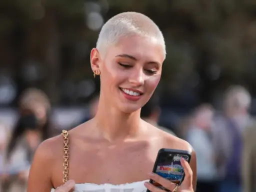 Junge Frau mit buzz cut blond, lächelnd und auf ihr Handy schauend.
