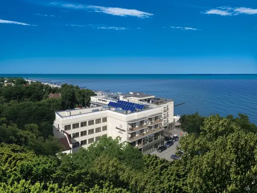 Nowoczesny hotel z panelami słonecznymi nad polskim morzem, otoczony zielenią.
