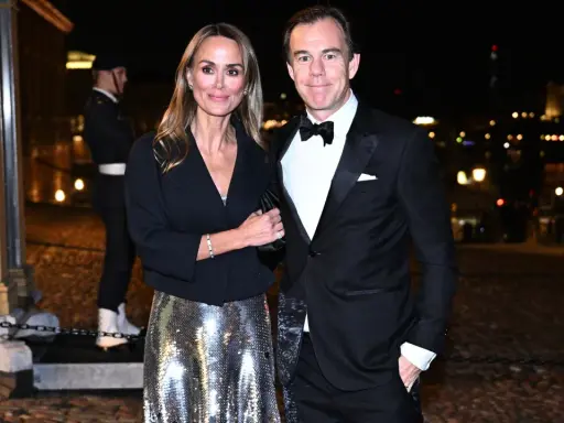 A couple in formal attire poses at night with a blurred city background.