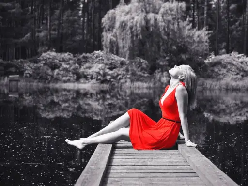 Mujer con vestido rojo sentada en muelle, efecto blanco y negro photoshop.