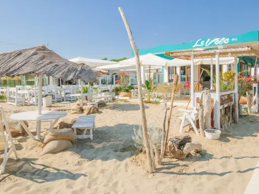 Un angolo di cervia strand con tavoli, sedie e ombrelloni di paglia, pronto ad accogliere i bagnanti.