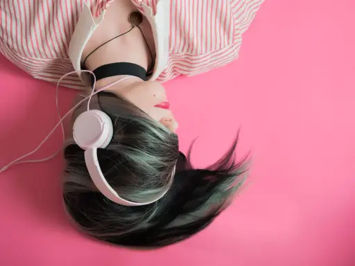 Jeune femme aux cheveux colorés, écouteurs blancs, sur fond rose. Une inspiration pour comment trouver un nom d'artiste.