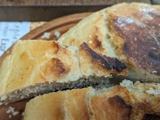 Ein knuspriges, goldbraunes dutch oven brot mit einer luftigen Krume, auf einem Holzbrett serviert.