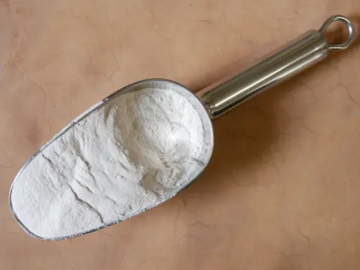 Une pelle métallique remplie de poudre blanche, peut-être de la colle gomme arabique, sur un fond texturé.