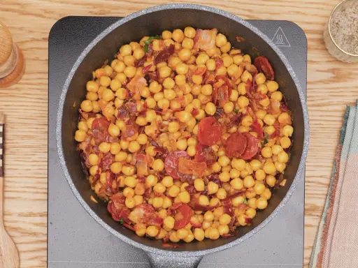 Garbanzos fritos con chorizo y bacon en sartén, listos para servir. Un plato sabroso y reconfortante.