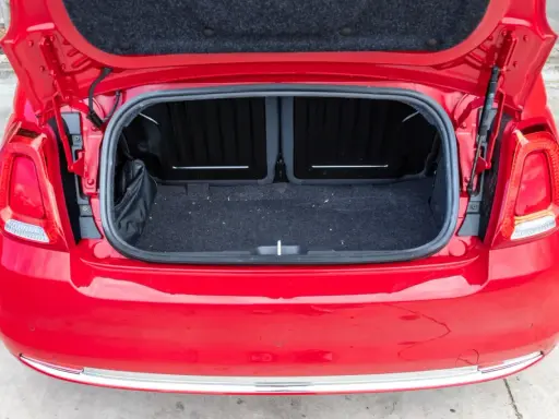 Maletero abierto de un Fiat 500 rojo, mostrando el espacio de carga cubierto de fieltro oscuro.