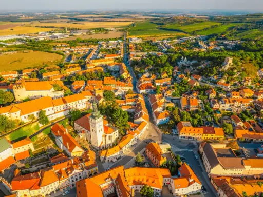 Malownicze miasteczko na Morawach w Czechach, z dominującą wieżą kościelną i pomarańczowymi dachami, otoczone zielonymi wzgórzami.