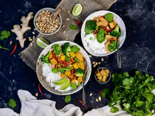 Zwei Schüsseln mit Reis, Tofu, Brokkoli und Erbsen. Ein Gericht, das vegan und proteinreich ist, mit Ingwer, Chili und Koriander garniert.