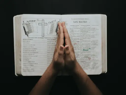 Dłonie złożone w modlitwie nad otwartą Biblią, z tekstami do modlitwy uwielbienia.