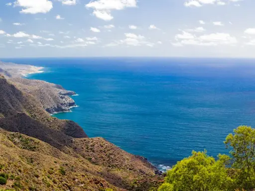 Blick auf die zerklüftete Küste und das tiefblaue Meer bei Cabo de Palos. Grüne Vegetation bedeckt die Hügel, die zum Meer abfallen.