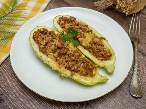 Dos mitades de calabacines rellenos de carne picada y queso gratinado, decorados con perejil. Un plato casero y delicioso.