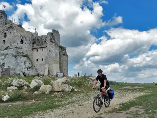 Rowerzysta na szlaku jura krakowsko częstochowska trasa, obok ruin zamku na skale.