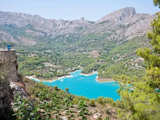 Espectacular vista de la ruta pueblos interior Alicante, con un embalse turquesa rodeado de montañas y vegetación.