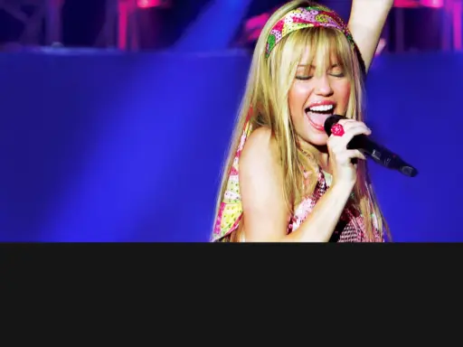 Miley Cyrus sjunger med ett stort leende på scenen i Sverige, iklädd en färgglad topp och pannband.