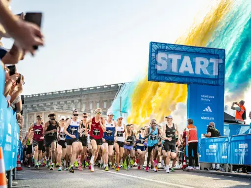 Löpare startar adidas halvmarathon i Stockholm. Publiken hejar och färgexplosioner lyser upp himlen.