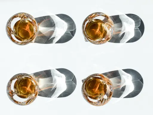 Vier Gläser mit bernsteinfarbenem Whiskey, die im Sonnenlicht stehen. Ein Vergleich zwischen Bourbon vs. Whiskey.