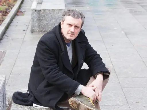 Uomo con cappotto nero seduto all'aperto, ricorda le atmosfere dei rocco schiavone libri.