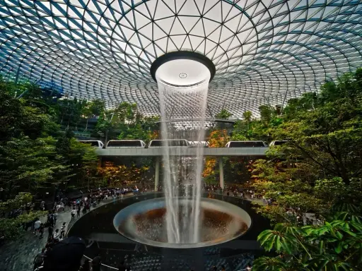 Wodospad HSBC Rain Vortex w porcie lotniczym Singapur-Changi, otoczony bujną zielenią i przejeżdżającymi pociągami.