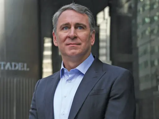 Ken Griffin, w eleganckim garniturze, stoi przed budynkiem z napisem "CITADEL".