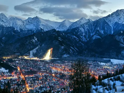 Oświetlone miasto Zakopane nocą, otoczone ośnieżonymi górami. Idealne miejsce na zakup biletów na zimowy wypoczynek.