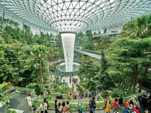Imponerande vattenfall och frodig grönska under glastaket på singapore flygplats. Människor njuter av den unika miljön.
