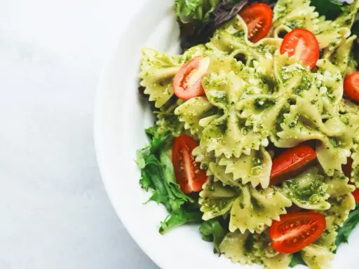 Pyszny makaron z pesto, udekorowany pomidorkami koktajlowymi i świeżą sałatą, podany na białym talerzu.
