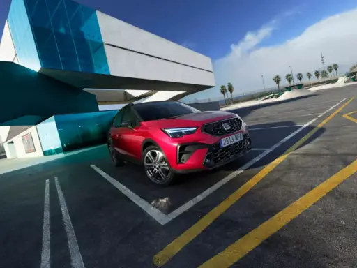 Czerwony Seat Arona, jeden z najnowszych seat modele, zaparkowany przy nowoczesnym budynku z niebieskimi akcentami.