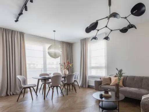 Nowoczesne oświetlenie salonu z jadalnią: designerski żyrandol i reflektory nad stołem. Aranżacje wnętrz z klasą.