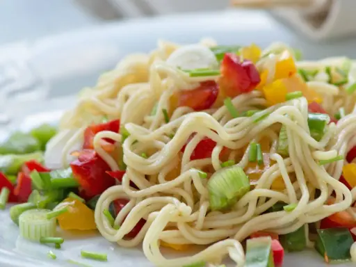 Ein bunter asia nudelsalat mit Paprika und Frühlingszwiebeln auf einem weißen Teller.