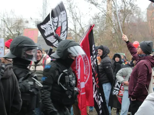 Demonstranten mit Fahnen, darunter eine mit der Aufschrift "System Metternich", und Polizisten in Schutzkleidung.