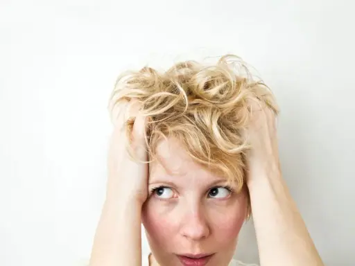 Kobieta z blond włosami, trzymająca się za głowę, z wyrazem zamyślenia i niepokoju, jakby doświadczała wahań nastroju związanych z cyklotymią.