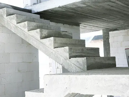 Surowe, betonowe schody czekają na wykończenie. W tle białe bloczki budowlane.