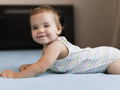 Un adorabile neonato di 8 mesi, con occhi azzurri e un sorriso contagioso, gioca sul letto.