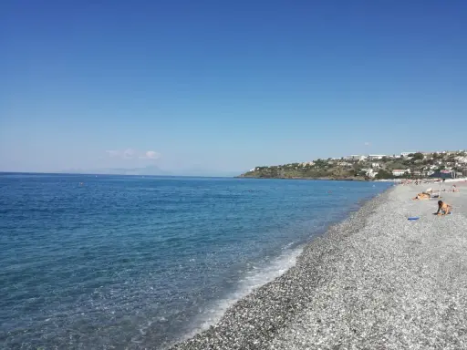Spiaggia di ciottoli con mare azzurro e case arroccate sulla collina. Una giornata perfetta per godersi la **scalinea mare**.