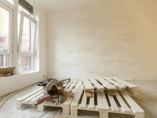 Herramientas listas para como pintar un palet. Madera blanca apilada, sierra ingletadora y pared con ladrillos blancos.