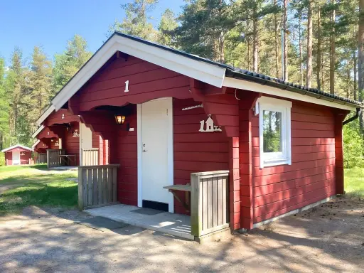 Röda stugor med vita knutar vid Gränna camping. En vit dörr och ett fönster syns på stuga nummer 1.