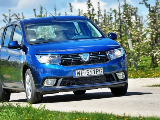 Niebieska Dacia Sandero 2025 jedzie przez kwitnący sad.