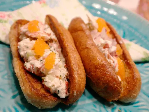 Två lyxiga lobster rolls med krämig fyllning, krispig gurka och orange rom på ett turkost fat.