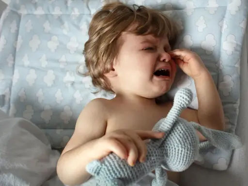 Kleines Kind weint im Schlaf, hält seinen Kuschelhasen fest. Tränen laufen über die Wangen, ein trauriger Moment.