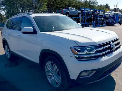 Biały VW Atlas stoi na parkingu, w tle widać lawetę z innymi samochodami.