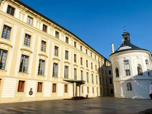 Zamek na Hradczanach, z jego długą, kremową fasadą i okrągłą, białą kaplicą, prezentuje się majestatycznie pod błękitnym niebem.