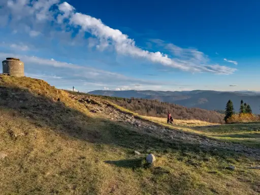 Na zboczu **blatniej góry** stoi betonowy bunkier. W oddali widać pasmo górskie i lasy.