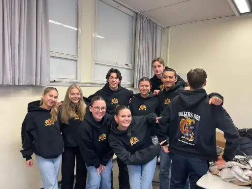 Acht lächelnde Schüler in schwarzen Hoodies mit dem Aufdruck "Volters Abi". Wie nennt man das Abitur noch?