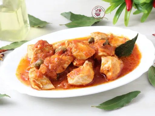 Succulento pollo alla pizzaiola con pomodoro, capperi e olive, guarnito con foglie di alloro e peperoncini secchi.