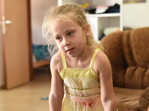 Zmartwiona dziewczynka w żółtej sukience. Co zrobić, gdy dziecko wstrzymuje mocz? Porady dla rodziców.