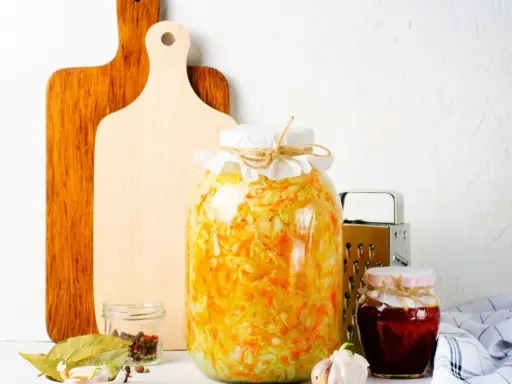 Großes Glas mit Sauerkraut, bereit zum **fermentieren im Schraubglas**. Daneben Gewürze, Knoblauch und ein kleines Glas Marmelade.