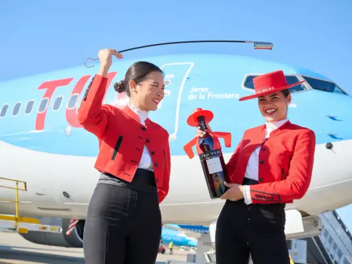 Zwei Frauen in Flamenco-Kleidung am Flughafen Jerez. Eine hält eine Flasche Tio Pepe Sherry, die andere eine Peitsche.