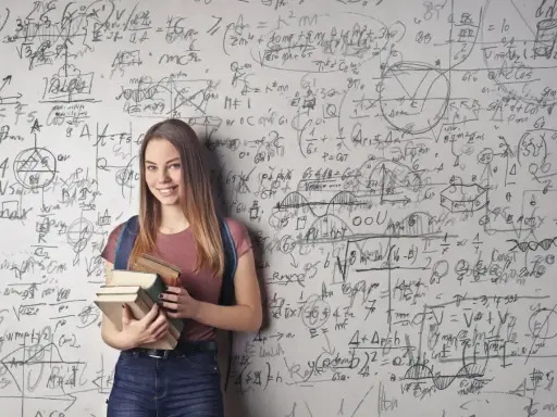 Uśmiechnięta studentka z książkami przed ścianą pełną równań matematycznych. Zastanawia się, co po studiach matematycznych.